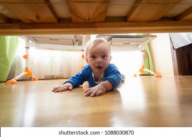 Portrait Of Amazed Toddler Boy Lying On Floor And Looking Under The Bed