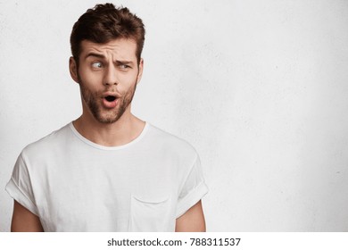 Portrait of amazed unshaven male wonders, raises eyebrows and opens mouth, has surprised expression, dressed casually, isolated over white background with copy space for your promotional text