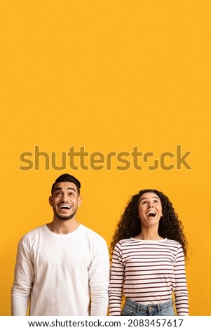 Portrait Of Amazed Young Arab Couple Looking Up With Opened Mouth, Dazed Middle Eastern Man And Woman Emotionally Reacting To Big Sale Or Nice Offer, Standing Over Yellow Background, Copy Space