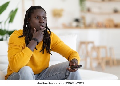 Portrait Of Amazed Young Black Guy Holding Remote Controller And Looking At Tv Screen, Shocked African American Man Watching Show On Television While Resting On Couch At Home, Copy Space