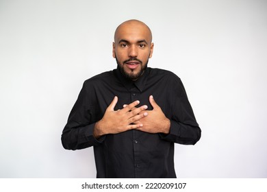 Portrait Of Amazed Young Man Pressing Hands To Chest. Happy Multiethnic Male Model With Bald Head In Black Shirt Looking At Camera, Mouth Open, Receiving Good News Or Gift. Surprise Concept