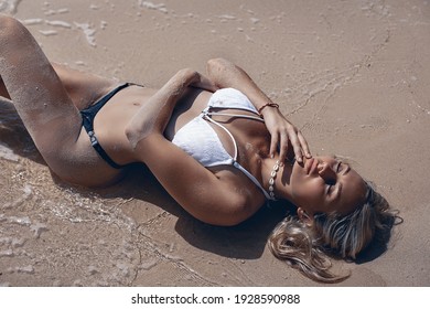 Portrait of an amazing fit girl in a blue and white bikini is lying on the golden sand of the beach. Sunbathing woman.