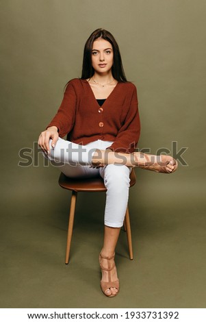 Portrait of Amazing young girl with a beautiful figure sitting on a chair against a olive background in the studio.