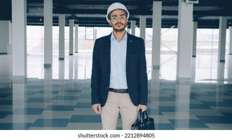 Portrait Of Ambitious Construction Investor In Helmet And Suit Standing In Empty Plant Building And Looking At Camera. Commercial Property And Investment Concept.