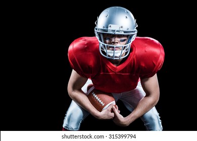 Portrait of American football player bending while holding ball against black background - Powered by Shutterstock