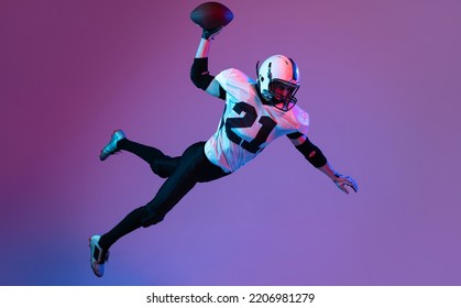 Portrait of american football player in motion, catching ball in a jump iisolated over purple background in neon light. Falling down. Concept of active life, team game, energy, sport, competition. - Powered by Shutterstock