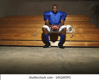 Portrait Of An American Football Player Sitting On Bench With Ball