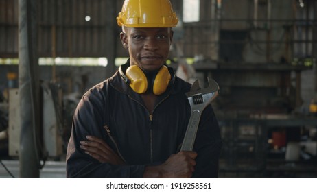 Portrait American Industrial Black Young Worker Man Smiling With Yellow Helmet In Front Machine, Engineer Standing Holding Wrench Tools And Arms Crossed At Work In The Industry Factory.