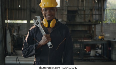 Portrait American industrial black young worker man smiling with helmet and ear protection in front machine, Engineer standing holding wrench on his shoulder at work in industry factory. - Powered by Shutterstock