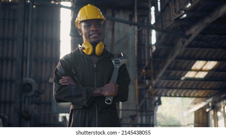 Portrait American industrial black young worker man smiling with yellow helmet in front machine, Engineer standing holding wrench tools and arms crossed at work in the industry factory. - Shutterstock ID 2145438055