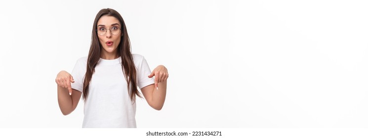 Portrait of amused and curious brunette female student inviting everyone check out very interesting event, follow this page or link, visit store, pointing fingers down, bottom advertisement. - Shutterstock ID 2231434271