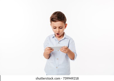 Portrait Of An Amused Cute Little Kid Playing Games On Smartphone Isolated Over White Background