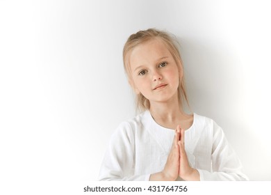 Portrait Of Angel-like European Child Joining Her Hand Like A Prayer With Tilted Head. Shinny And Pure Atmosphere Make Girl Look Pure And Balanced Like A Yogi In Mediation.