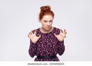 Portrait of angry aggressive young adult ginger woman wearing dress standing with raised arms and clenching teeth, expressing hate and anger. Indoor studio shot isolated on gray background. - Shutterstock ID 2310458231