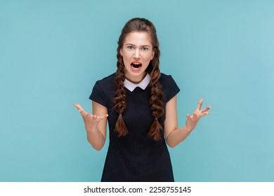 Portrait of angry attractive woman with braids standing with raised arms, screaming with anger and hate, arguing with somebody wearing black dress. woman Indoor studio shot isolated on blue background - Shutterstock ID 2258755145