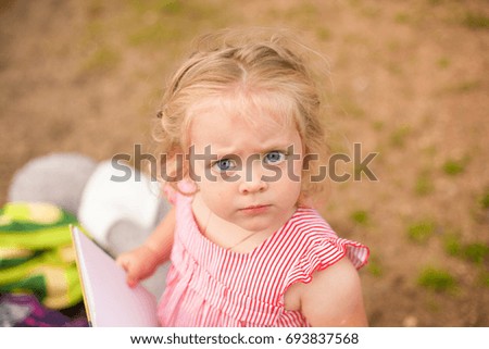 Portrait of angry baby girl looking at the camera, the book in his hands