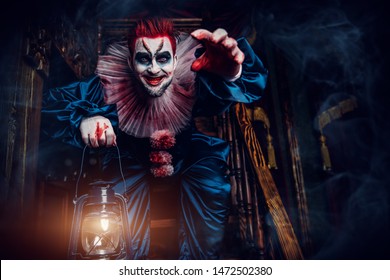A portrait of an angry crazy clown from a horror film with a lantern on the stairs. Halloween, carnival. - Shutterstock ID 1472502380