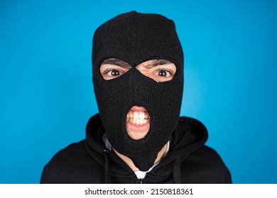 Portrait Of Angry Criminal Or Delinquent Wearing Black Ski Mask Isolated On Blue Background.