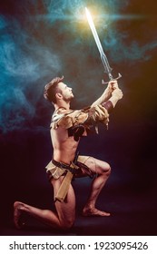 Portrait of angry gladiator with sword looking up against of black background. Isolated