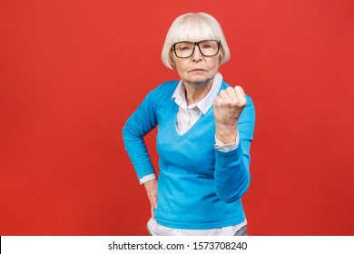 Portrait of angry grey haired old strict senior woman wearing glasses pointing up threatening with finger. Isolated over red background.