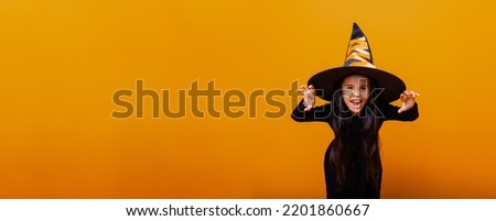 Portrait of an angry little girl in a witch costume, on a yellow background. halloween. banner