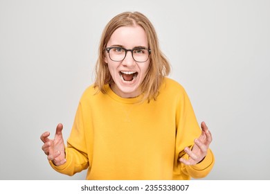 Portrait of angry schoolgirl yelling holding hands in furious gesture isolated on white studio background. Devil face. Human emotions, facial expression concept