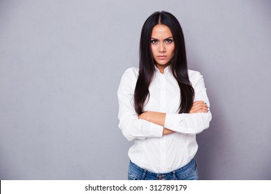 Portrait of angry woman standing with arms folded on gray background - Shutterstock ID 312789179
