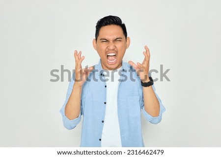 Portrait of angry young Asian man in casual clothes raising hands and screaming with aggressive expression isolated on white background