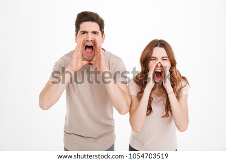 Portrait of an angry young couple screaming together isolated over white background
