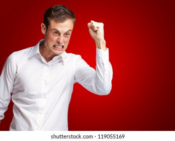 Portrait Of Angry Young Man Clenching His Fist On Red Background