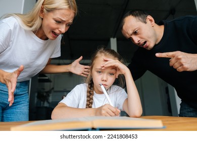 Portrait of angry young parents yelling and scolding together lazy little daughter sitting at table, doing homework, sad looking at camera. Concept of parent disciplining child for bad education. - Powered by Shutterstock