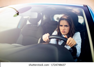 Portrait, angry young sitting woman pissed off by drivers in front of her and gesturing with hands. Road rage traffic jam concept. Woman is driving her car very aggressive and gives gesture with his f