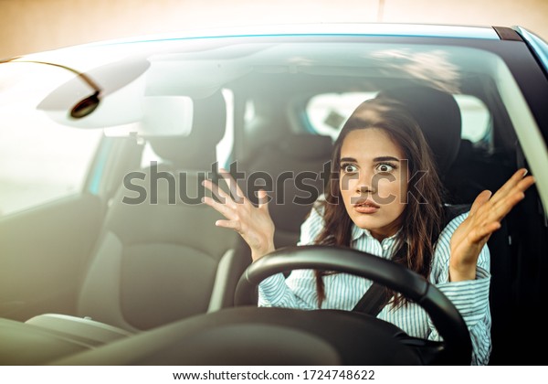 Portrait, angry young sitting woman pissed off by\
drivers in front of her and gesturing with hands. Road rage traffic\
jam concept. Woman is driving her car very aggressive and gives\
gesture with his f