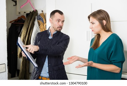 Portrait of annoyed debt collector and shocked young woman with overdue payment at home doorway

