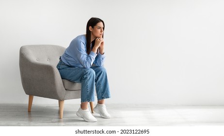 Portrait of annoyed young lady sitting in armchair against white studio wall, banner design with free space. Millennial woman feeling angry and stressed, having bad mood or depression - Shutterstock ID 2023122695