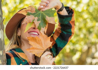Portrait Of An Anonymous Young Woman Covering Her Face With Dried Leaves, Only A Pretty Smile Is Visible. Close-up Of A Smiling Woman With Autumn Leaves On Her Face.