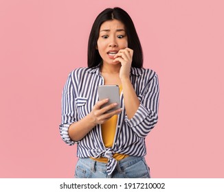 Portrait of anxious scared asian young woman looking at mobile phone seeing bad news, photos or message. Worried lady biting nails isolated on pink studio wall background. Human reaction, expression - Powered by Shutterstock