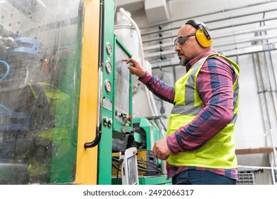 Portrait of apprentice engineering worker mature machine operator man pressing programming buttons on the control board panel of CNC machine in factory