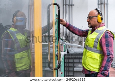 Portrait of apprentice engineering worker mature machine operator man pressing programming buttons on the control board panel of CNC machine in factory