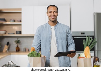 Portrait Of Arabian Handsome Young Husband, Man Searching Menu Recipe Of Healthy Vegetarian Vegetable Salad In Digital Tablet In Modern Bright Kitchen At Home. Happy Arab Male And Technology Concept.