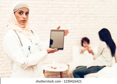 Portrait Of Arabic Female Doctor Holding Ipad. Arabic Female Pediatrician Wearing Hijab. Hospital Concept. Healthy Concept. Pediatrician Writes A Prescription. Child Patient Visiting Doctor.