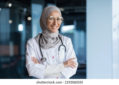 Portrait of Arabic female doctor in modern clinic, Muslim woman wearing hijab glasses and white medical coat working in hospital office, smiling and looking at camera with crossed arms - Powered by Shutterstock