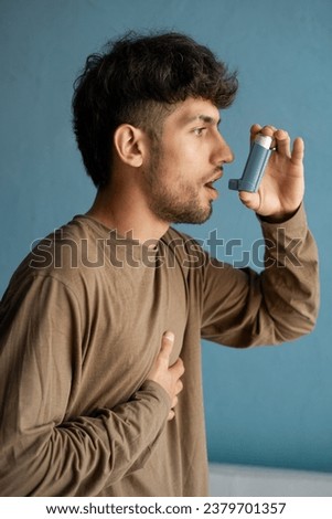 portrait of arabic young man using asthma inhaler against blue background at home. Close-up