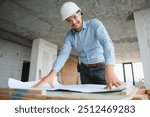 Portrait of an architect builder studying layout plan of the rooms, civil engineer working with documents on construction site, building and home renovation, professional foreman at work