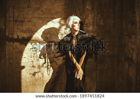 Portrait of an aristocratic old widow woman in a rich black dress standing sad by the ruined wall and looking to the window. Black Widow. Fantasy World. Halloween.