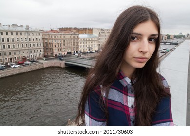 portrait of an Armenian girl with fluttering long dark hair in a checkered shirt and jeans on a rooftop in  St. Petersburg