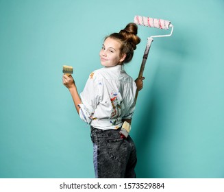 Portrait artist decorator at work  Young woman in shirt and paint stains is standing back at the wall and paint roller   brushes  looking over her shoulder at us