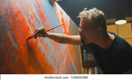 Portrait of Artist Working on Abstract Painting, Uses Paint Brush To Create Daringly Emotional Modern Picture. Dark Creative Studio Large Canvas Stands on Easel Illuminated. Side View Close-up Shot - Powered by Shutterstock