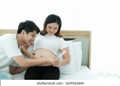 portrait asia young pregnant woman and husband happy together on the bed with ultrasound photo - Shutterstock ID 1659562444
