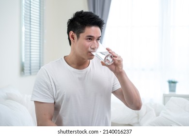 Portrait Of Asian Attractive Male Holding A Glass Of Water In Kitchen. Young Thirsty Handsome Man Pouring And Drink Clean Mineral Natural In Cup After Wake Up In Early Morning For Health Care In House